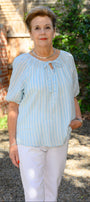Front view a light blue striped shirt and white pants.