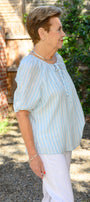 Side view a light blue striped blouse and white pants.