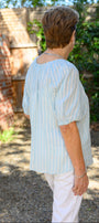 Back view a light blue striped shirt and white pants.