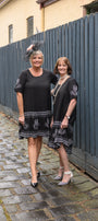 Two women in black dresses standing on a cobblestone path next to a wooden fence.