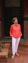 Woman in a orange  sweater and white pants.