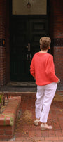 Back view a orange sweater and white pants.