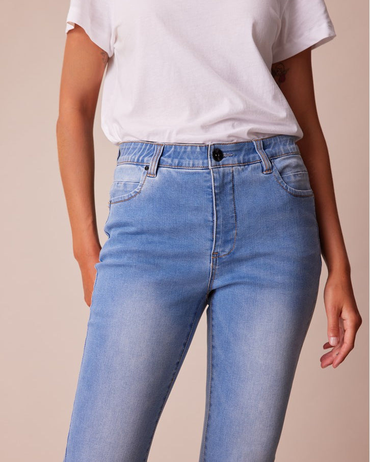 A person wearing light blue high-waisted skinny jeans and a white t-shirt, shown from the chest down against a solid beige background.