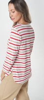 A woman wearing a long-sleeve striped top with red, beige, and white horizontal stripes, paired with beige pants, shown from a side-back angle against a light gray studio background.