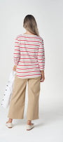 A woman is shown from behind wearing a red and white striped long-sleeve top, beige wide-leg cropped pants, and white shoes, holding a white bag against a plain white studio background.