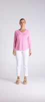 A woman modeling a light pink long-sleeve V-neck top and white cropped pants against a light gray studio background.