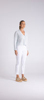 A woman modeling a light blue and white striped long-sleeve wrap top with white cropped pants and beige sandals, standing against a light gray studio background.