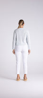 A woman viewed from behind wearing a light blue ribbed knit sweater and white cropped pants, standing against a plain light gray studio background.