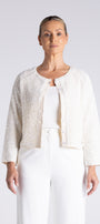 A woman modeling a cropped, textured cream jacket with three-quarter sleeves over a matching white top and white trousers, shot against a light gray studio background.