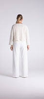 A model shown from the back wearing a textured cream knit sweater and white wide-leg trousers, standing against a light gray studio background.