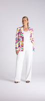 A woman modeling a white wide-leg jumpsuit with a colorful abstract print blazer, standing against a light gray studio background.