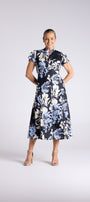 A woman modeling a short-sleeve midi dress with a navy blue, light blue, and white floral pattern, standing against a light gray studio background.