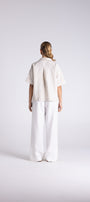 A model viewed from behind wearing a short sleeve cream linen shirt and matching wide leg linen trousers against a light gray studio background.