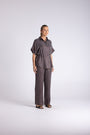 A woman modeling a dark gray two-piece linen set consisting of a short-sleeve button-up shirt and matching wide-leg trousers, standing against a light gray studio background.