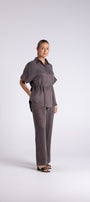 A woman modeling a dark grey short sleeve jumpsuit with a cinched waist and wide leg pants, standing against a light grey studio background.
