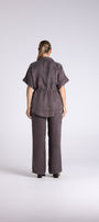 A model viewed from the back wearing a dark brown short sleeve collared shirt and matching wide leg trousers against a light gray studio background.