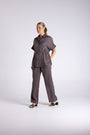 A woman modeling a dark gray short-sleeve button-up shirt and matching wide-leg trousers, standing against a light gray studio background.