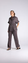 A woman modeling a dark gray short sleeve button up shirt and matching wide leg trousers, standing against a light gray studio background.