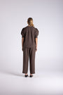 A model viewed from the back wearing a dark brown short-sleeve top with puffed shoulders and matching wide-leg trousers, standing against a light gray studio background.