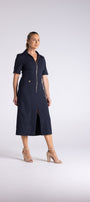 A woman modeling a dark navy midi shirt dress with short sleeves, a front zipper, and a front slit, paired with beige heeled sandals, against a light gray studio background.