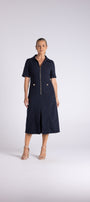 A woman modeling a dark navy blue short-sleeve midi dress with a front zipper and gold-tone hardware, standing against a light gray studio background.