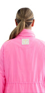 A woman viewed from behind wearing a bright pink jacket with a small square patch on the upper back, isolated on a white background.