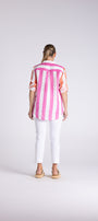 A woman viewed from behind wearing a pink and white vertically striped short-sleeve button-up shirt, white cropped pants, and tan sandals, standing against a light gray studio background.