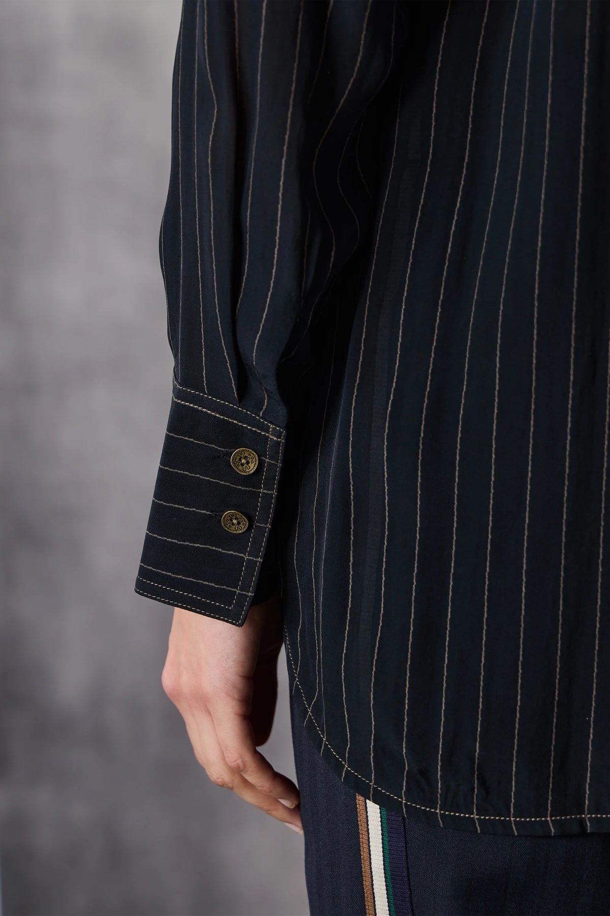 Close up of a dark pinstripe shirt with button cuffs on a grey background
