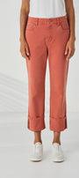 Front view  of cropped, cuffed denim jeans in a muted terracotta or dusty rose color, paired with a white top and white sneakers.