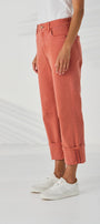 Sid View high waisted, cropped cuffed jeans in a dusty rose or terracotta colour, paired with white sneakers, shown from the waist down.