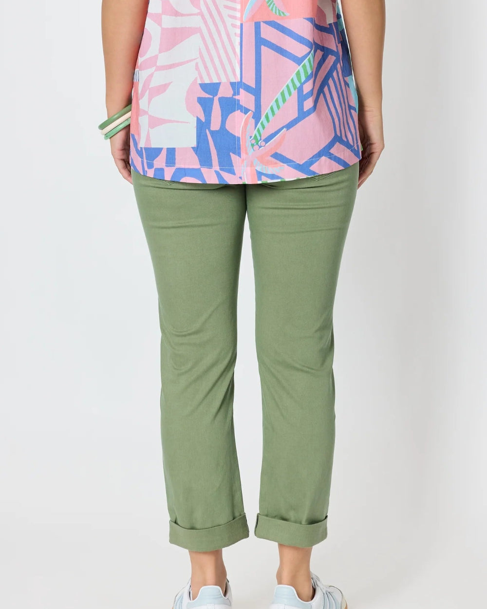  back view olive green cropped pants with rolled cuffs, a coloruful patterned top, and white sneakers .