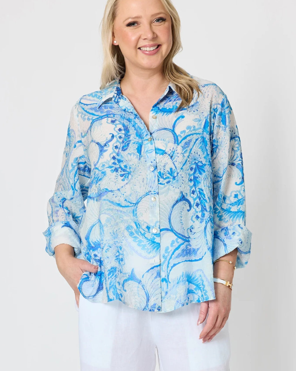 light blue and white paisley print button up blouse with white pants.