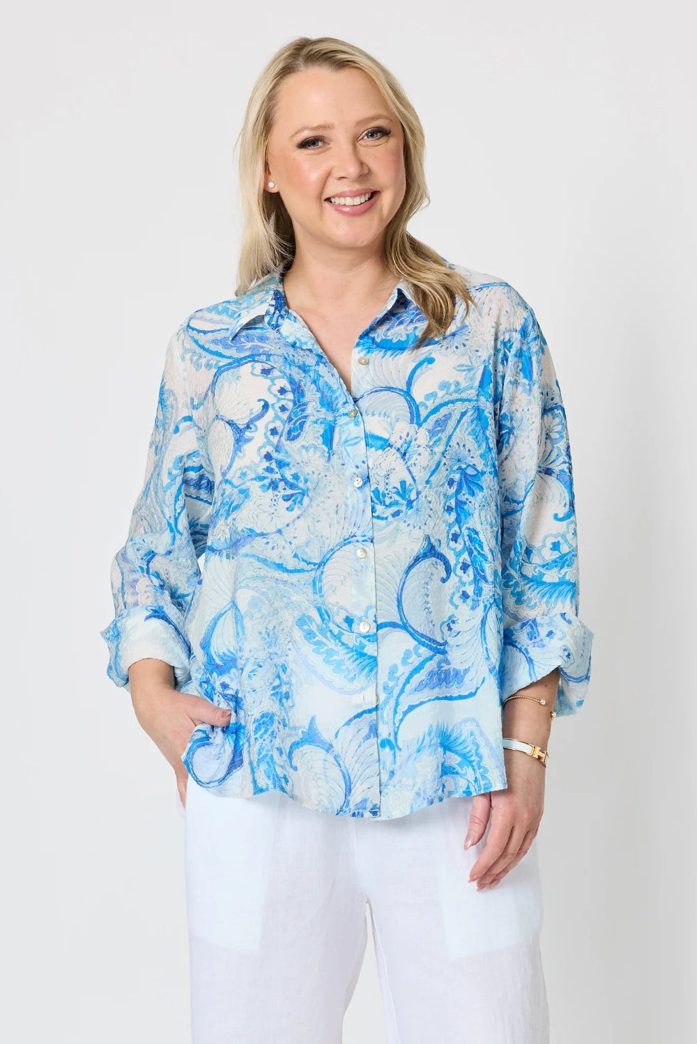 light blue and white paisley print button up blouse with white pants.