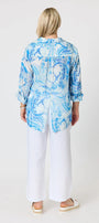 A woman viewed from the back wearing a light blue and white abstract print long sleeve blouse with white wide leg pants and white espadrille sandals.