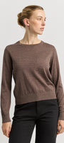 Woman wearing a brown sweater and black pants on a light gray background