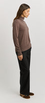 Woman wearing a brown turtleneck sweater and black pants on a light gray background