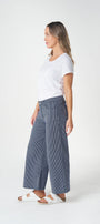 A woman shown in profile wearing a white short-sleeve T-shirt, wide-leg blue jeans, and white slide sandals against a clean white studio background.