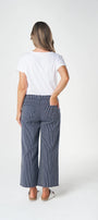 A woman is shown from behind wearing a white t-shirt and slate blue wide-leg cropped pants against a plain white studio background.
