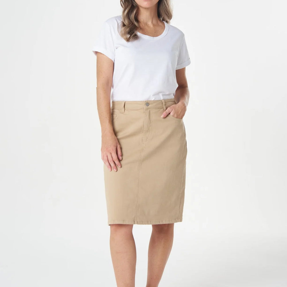 A woman modeling a beige knee-length skirt with a white t-shirt and white sneakers, standing against a plain white studio background.