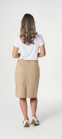 A woman viewed from behind wearing a white short-sleeve t-shirt, a beige knee-length skirt, and white sneakers with brown heels, standing against a light gray studio background.