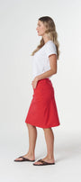 A woman in profile wearing a white short-sleeve t-shirt, a bright red A-line midi skirt, and dark brown sandals, standing against a light gray studio background.