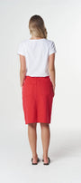 A woman viewed from behind wearing a white short-sleeve top and a bright red knee-length skirt with front patch pockets, standing against a light gray studio background.