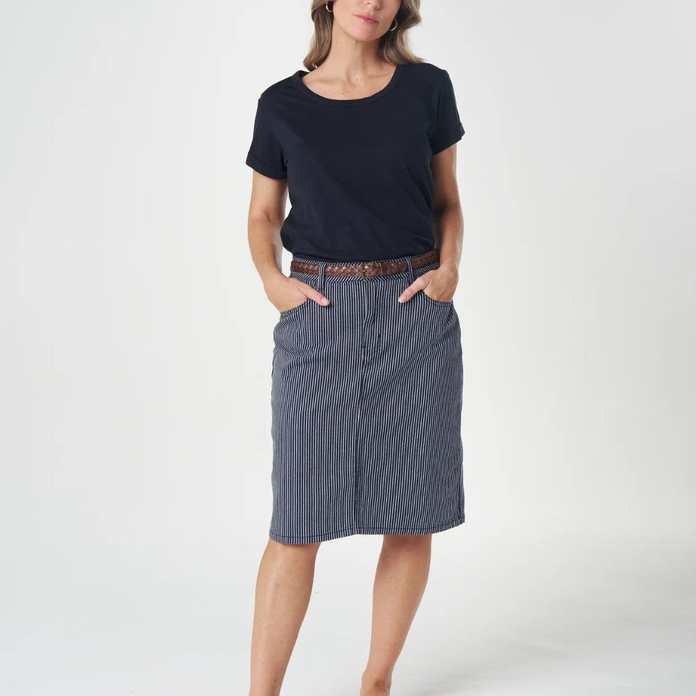 A woman modeling a dark navy blue short-sleeve t-shirt and a slate blue-gray knee-length skirt, styled with a brown belt and black sandals, against a plain white studio background.