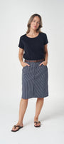 A woman modeling a dark navy blue short-sleeve t-shirt and a slate blue-gray knee-length skirt, styled with a brown belt and black sandals, against a plain white studio background.