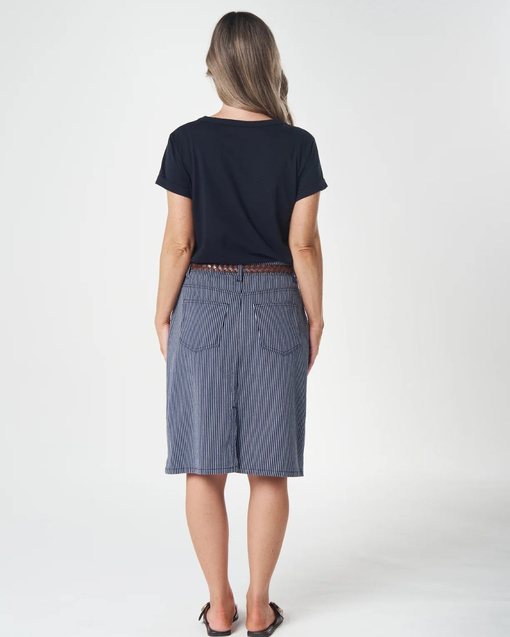 A woman is shown from behind wearing a navy blue short-sleeve t-shirt and a blue denim skirt, standing against a plain white studio background.