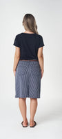 A woman is shown from behind wearing a navy blue short-sleeve t-shirt and a blue denim skirt, standing against a plain white studio background.