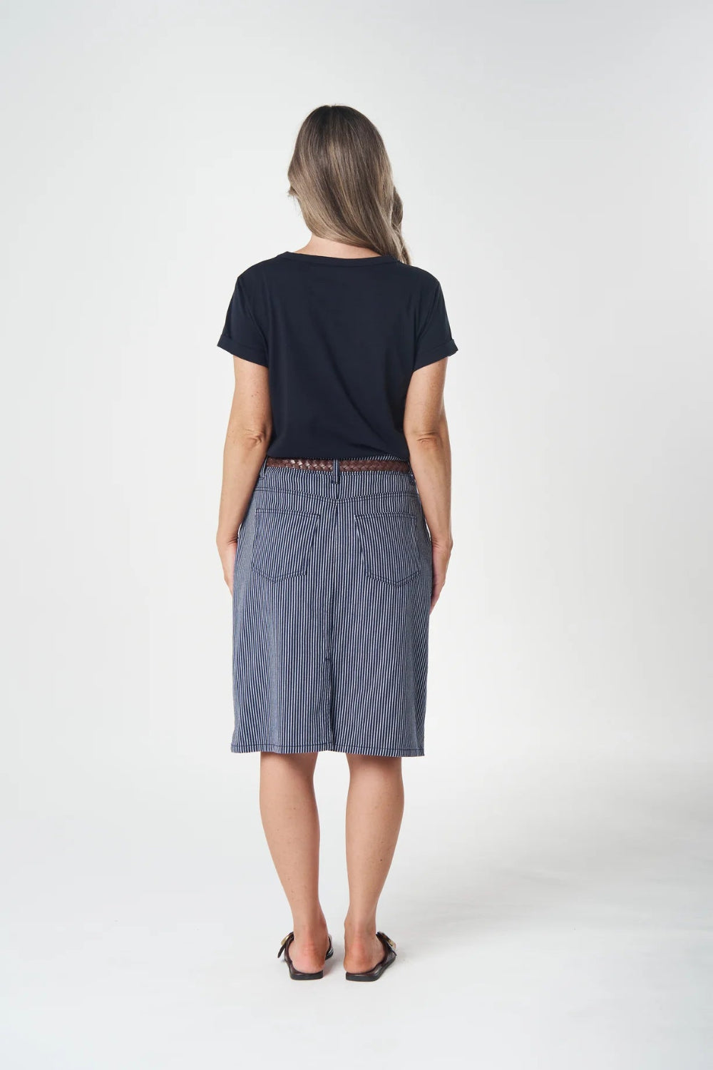 A woman is shown from behind wearing a navy blue short-sleeve t-shirt and a blue denim skirt, standing against a plain white studio background.