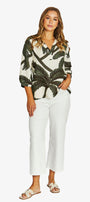 A woman modeling a white long-sleeve blouse with a dark green palm leaf pattern, paired with white cropped pants and beige slide sandals, against a light gray studio background.