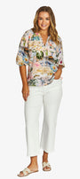 Front View  short sleeve button up blouse with a colourful tropical floral print, paired with white cropped pants and beige slide sandals.