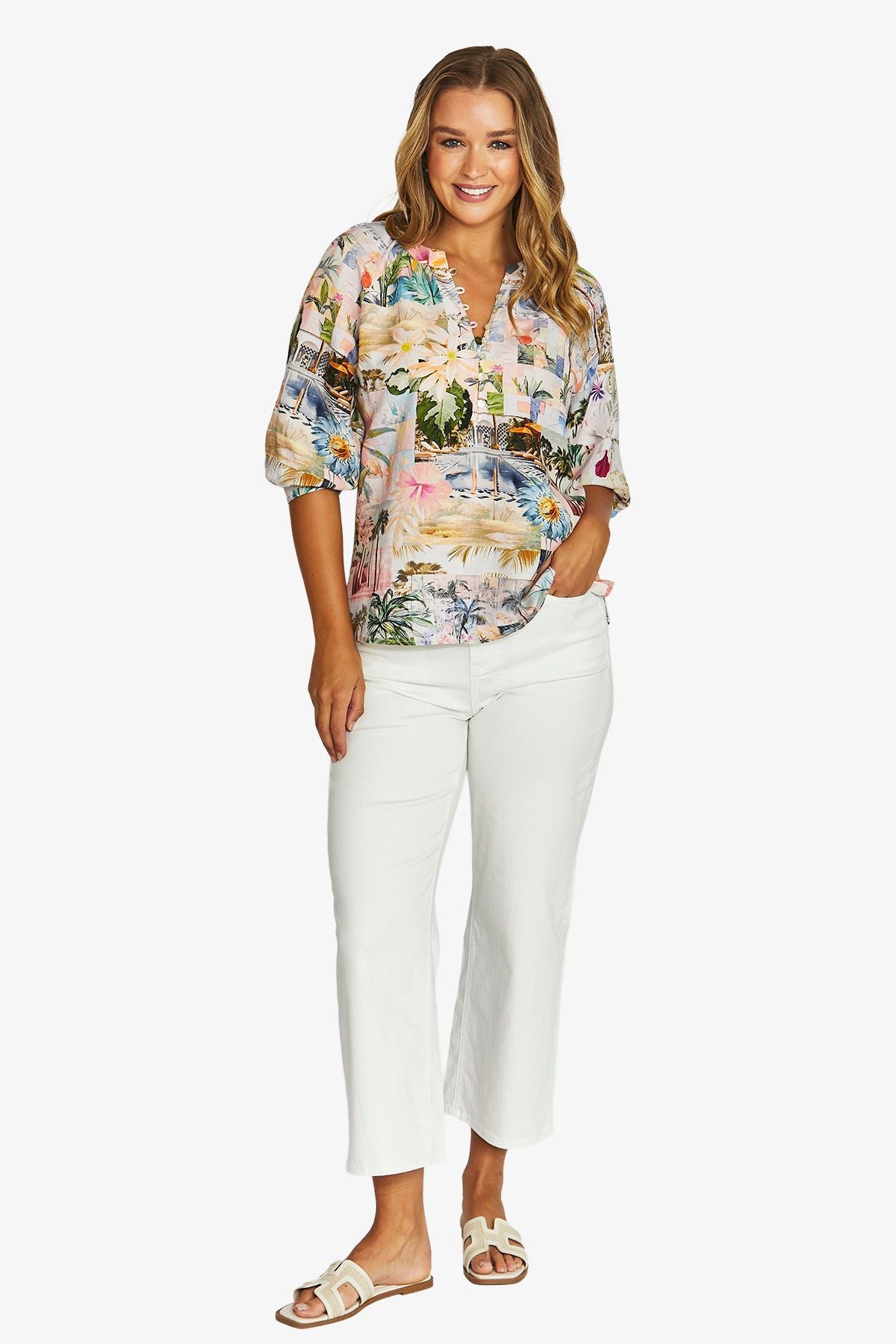 Front View  short sleeve button up blouse with a colourful tropical floral print, paired with white cropped pants and beige slide sandals.